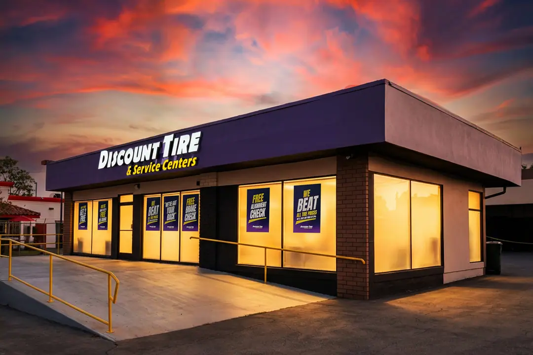 The Discount Tire & Service Centers storefront in Downey at dusk, with its purple fascia sign and lit service-bay windows